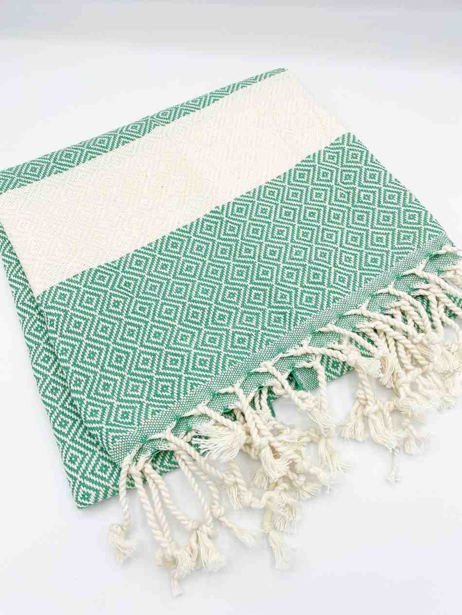 Green hand towel with white diamond pattern and knotted fringe edges on white background