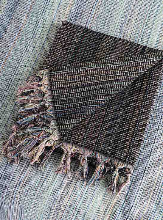 Folded black king size blanket with fringe tassels and multicolor woven pattern
