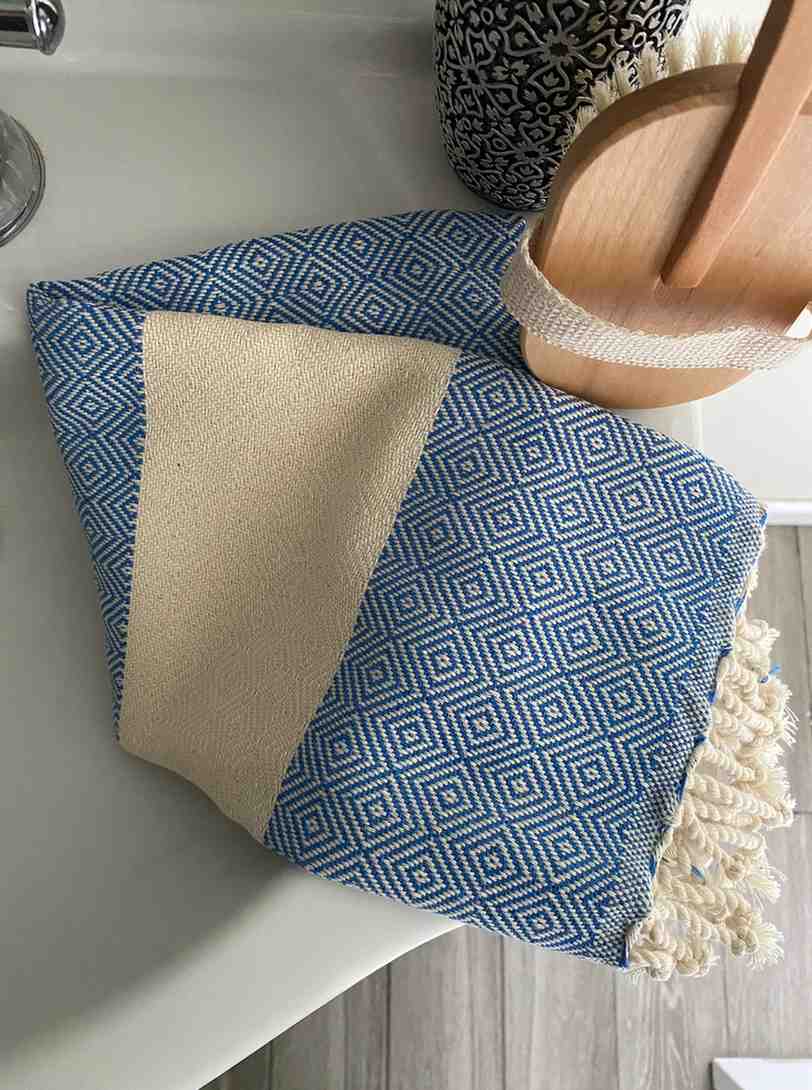 Blue diamond pattern hand towel folded on a sink with cream fringe and bath accessories