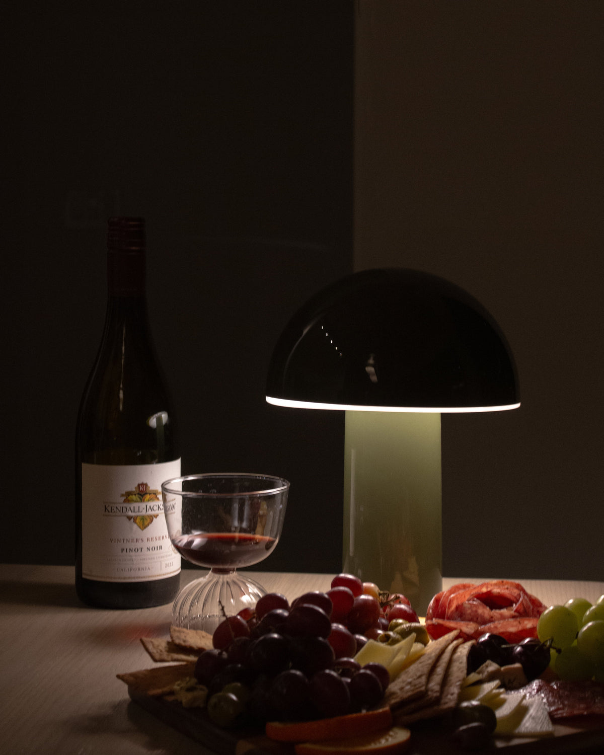 Wine bottle, glass, and charcuterie board with a lamp on a dark background