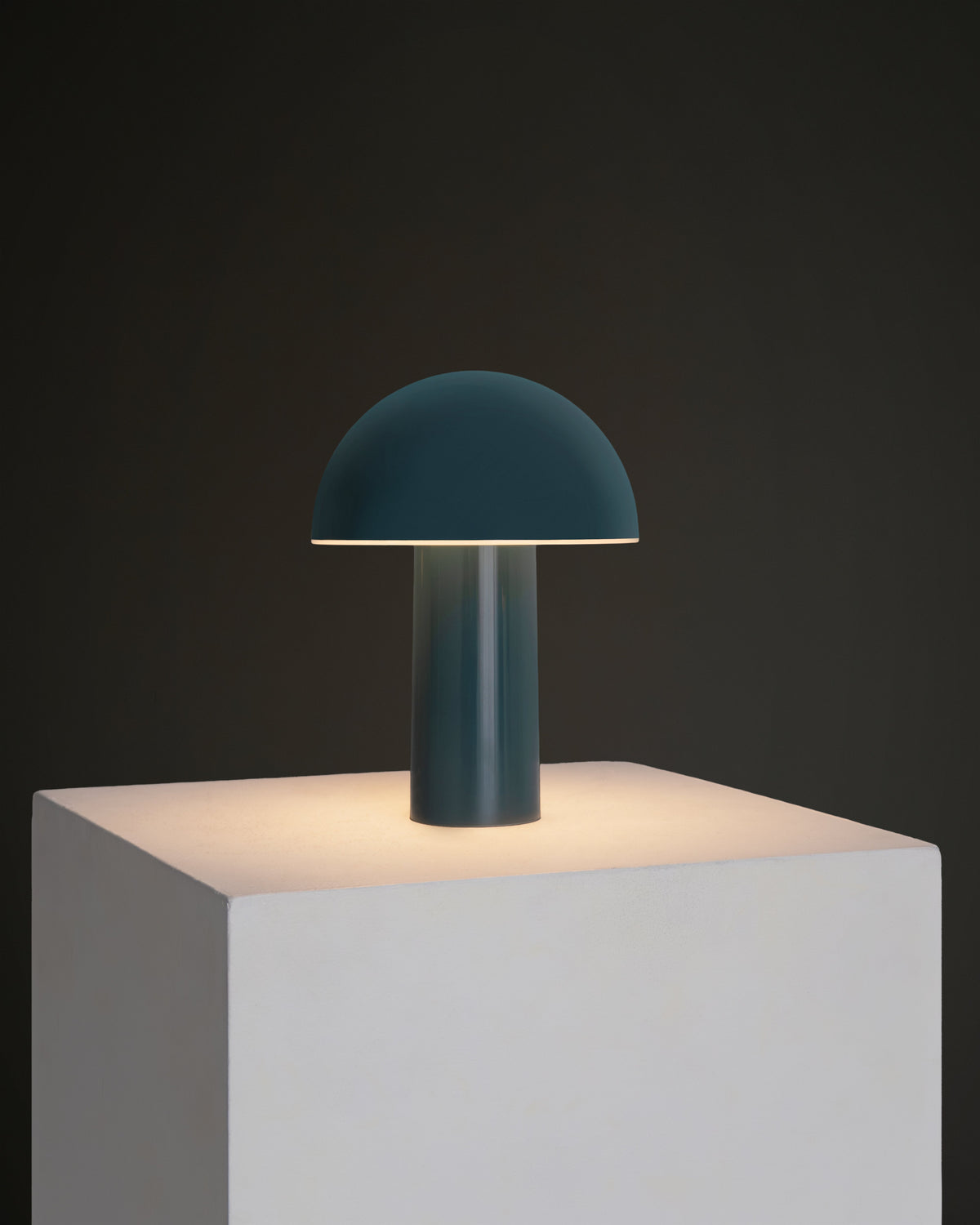 blue table lamp on a gray pedestal against a dark background