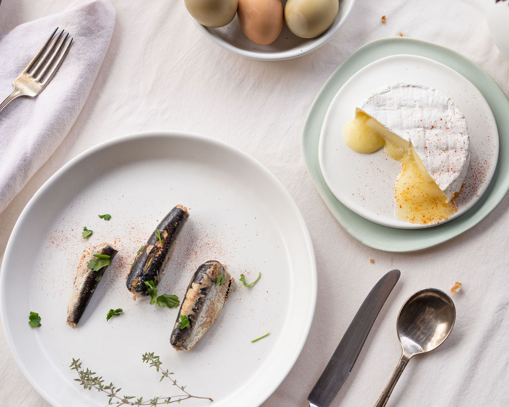 Dinner setting with mussels on a white plate, a dessert on a smaller plate, and cutlery on a light surface.