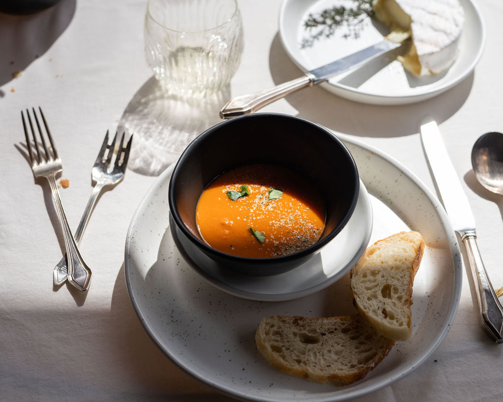 Black bowl of soup with bread slices on a white table setting