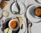 Two bowls of soup with bread and herbs on a white table.