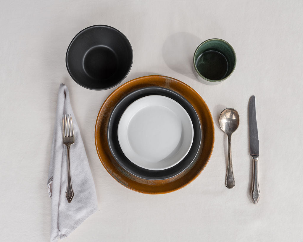 Dinnerware set with bowls, plates, and cutlery on a light gray surface