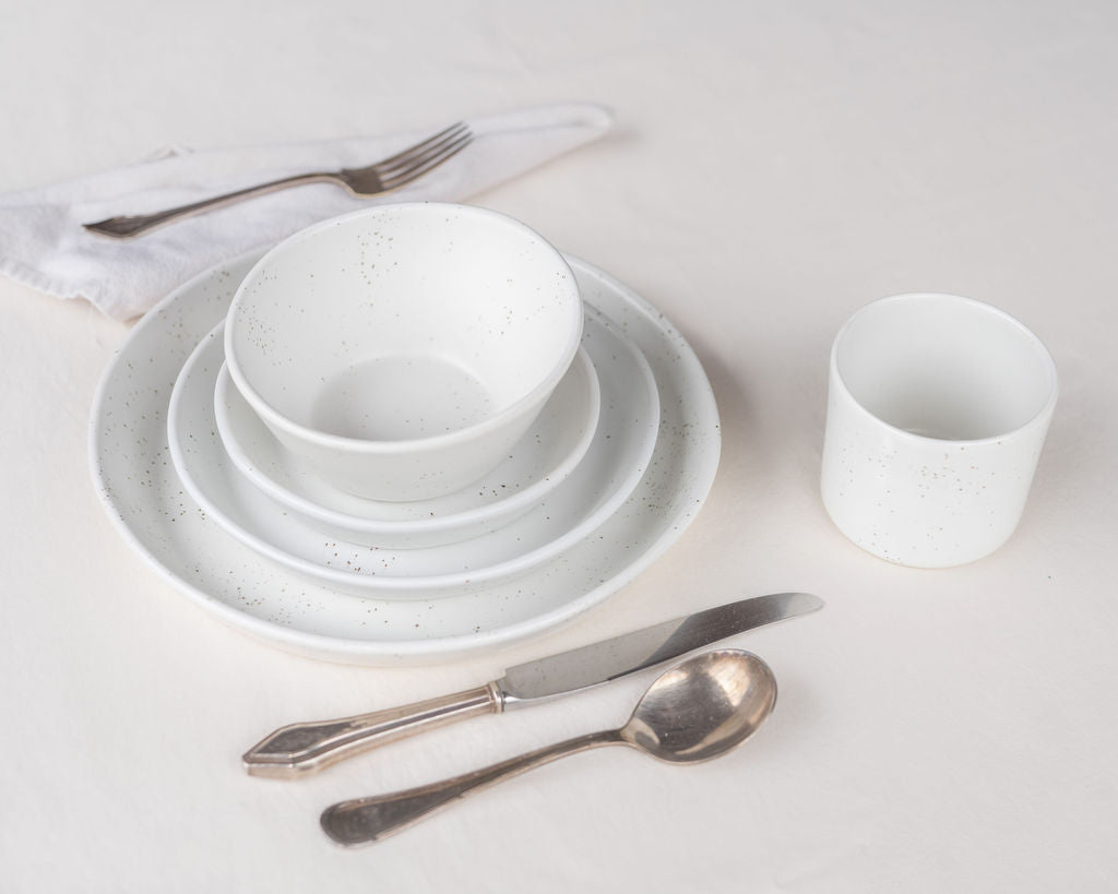 White ceramic dinnerware set with silver cutlery on a light gray background