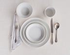 White ceramic dinnerware set with silver cutlery on a light gray background