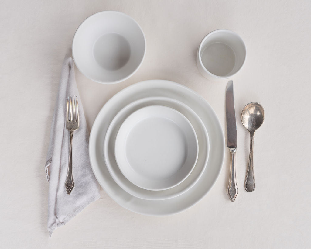 White ceramic dinnerware set with silver cutlery on a light gray background