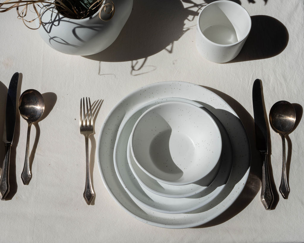 Set of white ceramic plates with silverware on a light surface