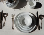 Set of white ceramic plates with silverware on a light surface