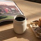 White ceramic mug with coffee on a wooden table next to a magazine and snacks