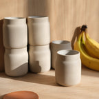 Set of beige ceramic cups on a wooden surface with bananas in the background