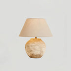 Table lamp with textured base and beige lampshade on a light gray background