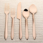 Set of rose gold cutlery including fork, knife, and spoons on a textured surface.