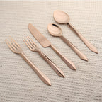 Rose gold cutlery set on a textured beige surface