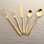 Set of gold cutlery including forks, knives, and spoons on a textured beige surface.
