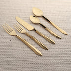 Set of gold cutlery including knife, fork, and spoons on a textured surface