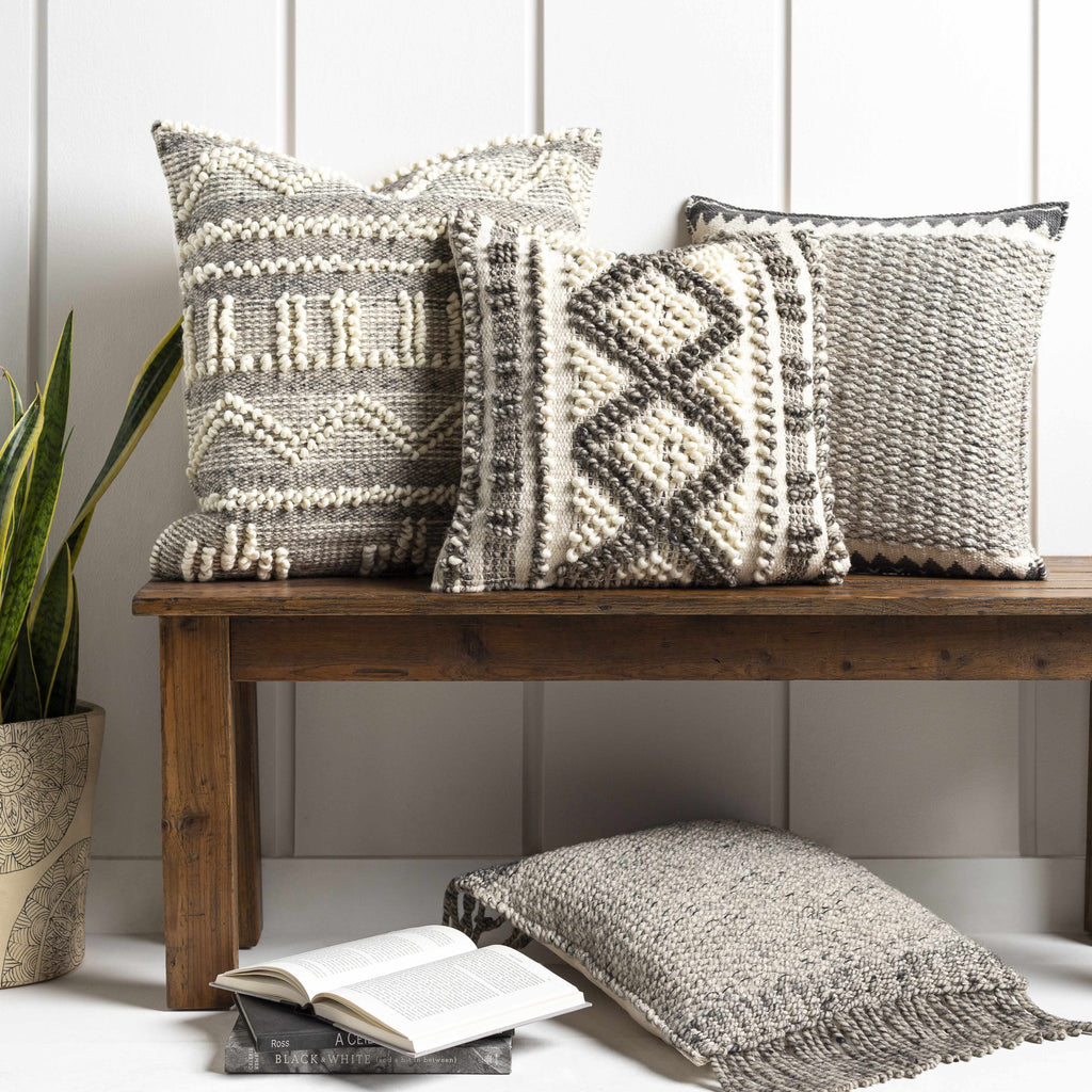 Three patterned pillows on a wooden bench with a plant and book in the background.