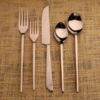 Set of silver cutlery including forks, a knife, and spoons on a textured beige background.