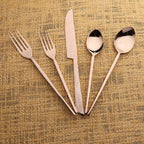 Set of bronze cutlery including forks, a knife, and two spoons on a textured beige background.