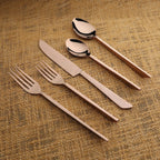 Set of silver cutlery including a fork, knife, and two spoons on a textured brown surface.