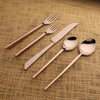 Set of rose gold cutlery including fork, knife, and two spoons on a textured brown surface.