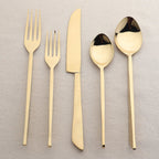 Set of gold cutlery including forks and spoons on a textured beige surface