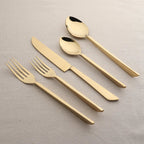 Set of gold cutlery including knives, forks, and spoons on a beige background