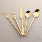 Set of gold cutlery including forks, knives, and spoons on a beige background