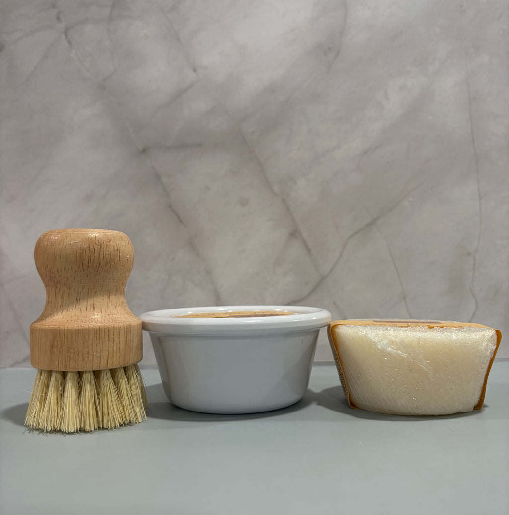 Wooden brush, white container, and beige soap on a marble surface