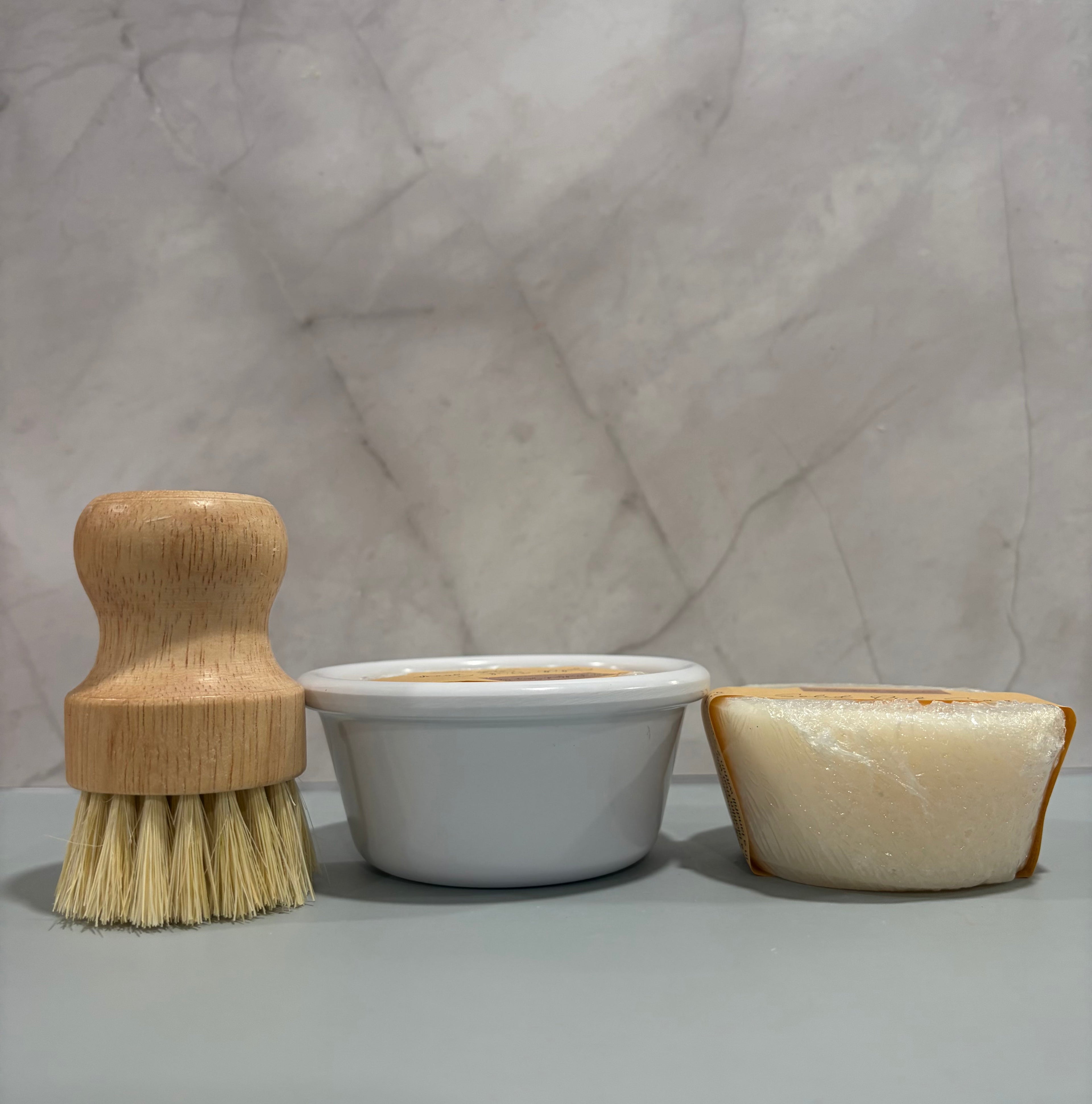 Wooden brush, white container, and beige soap on a marble surface