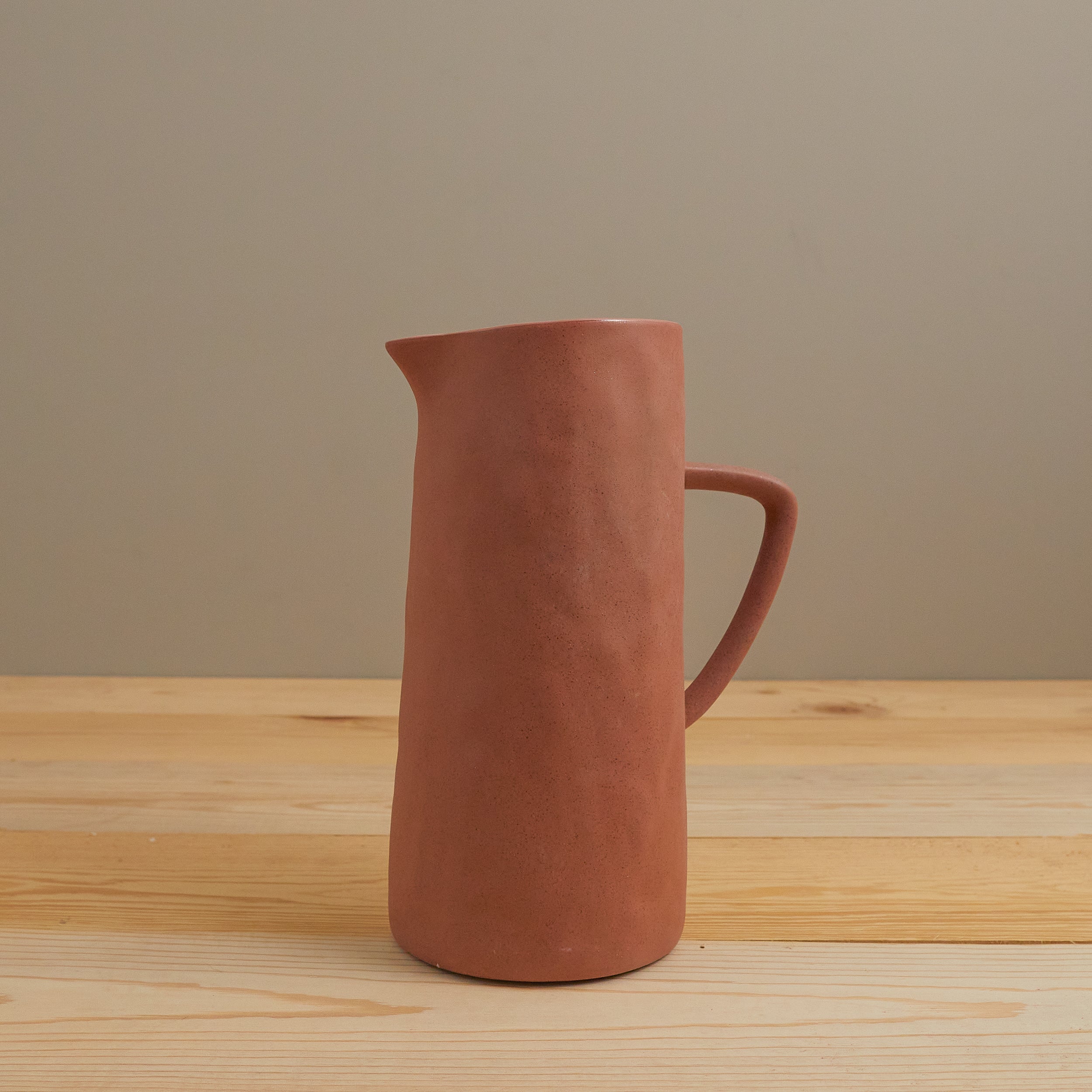 Terracotta pitcher on a wooden surface with a plain background