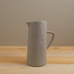 Gray ceramic pitcher on a wooden surface with a beige wall background