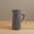 Gray pitcher on a wooden surface with a beige background