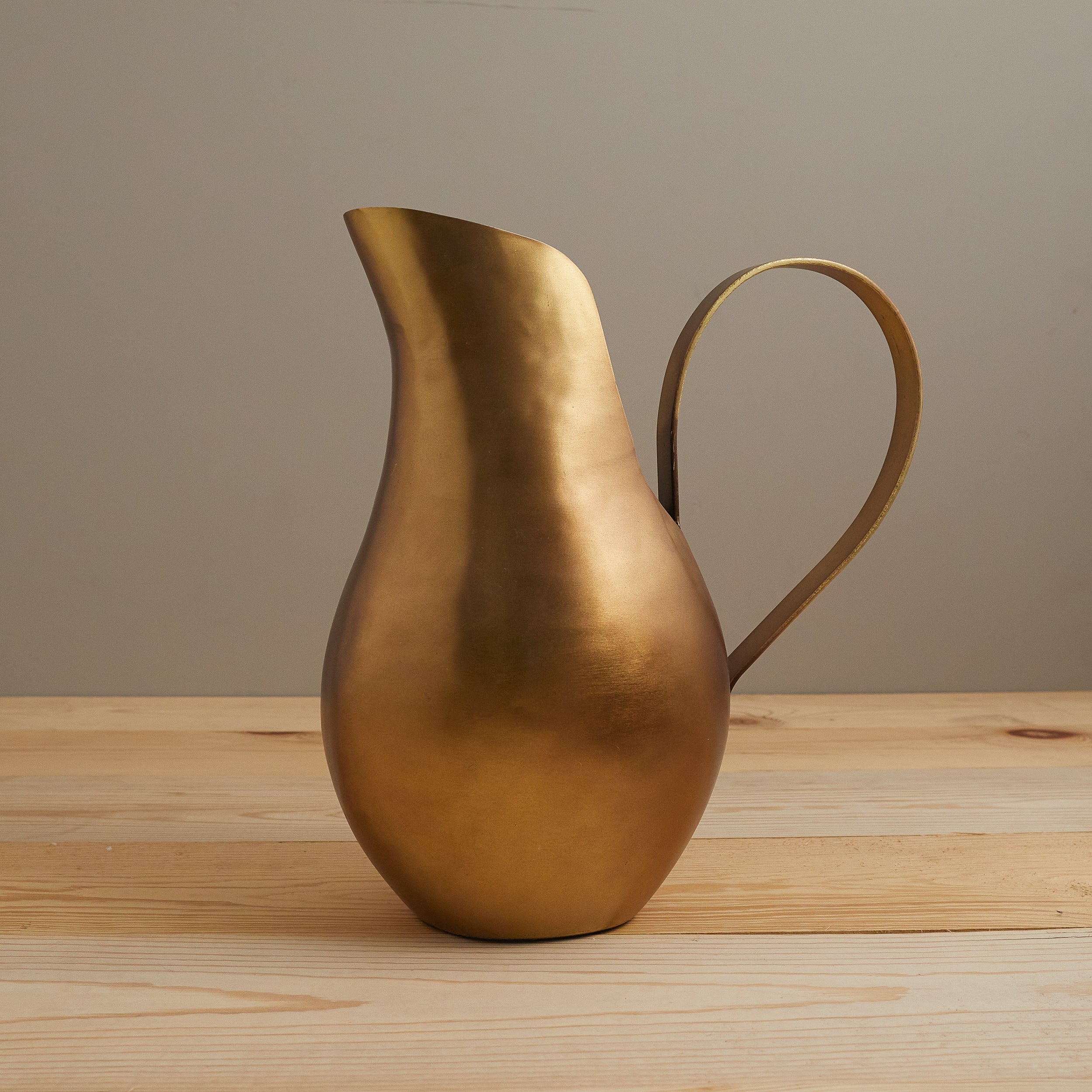 Bronze pitcher on a wooden surface with a neutral background