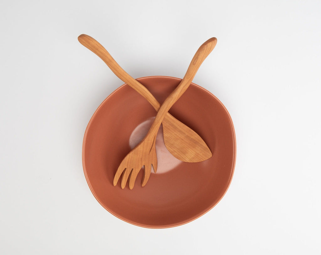 Wooden fork and spoon on a terracotta bowl against a white background