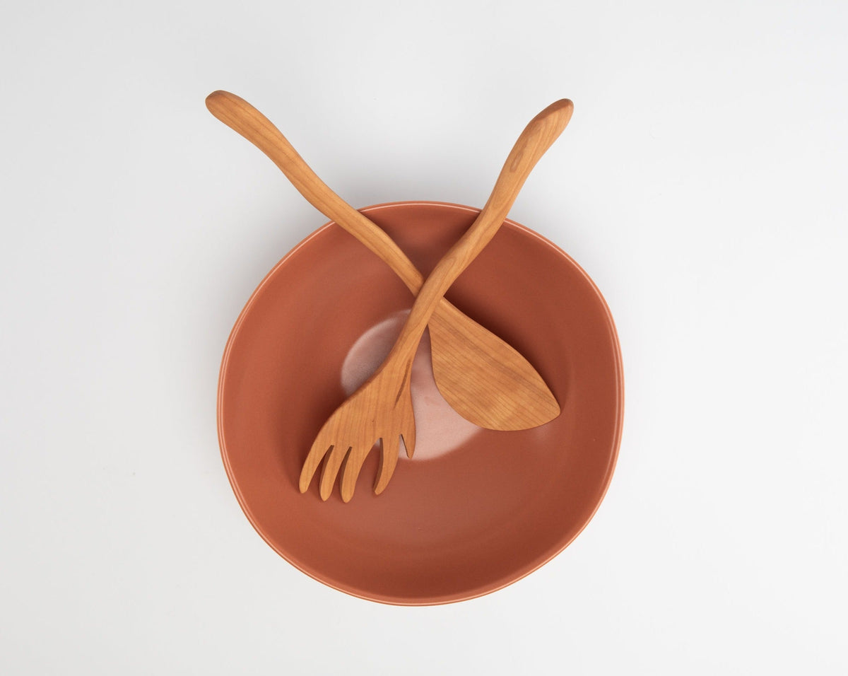 Wooden fork and spoon on a terracotta bowl against a white background