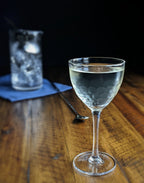 Clear wine cocktail glass with a drink on a wooden table with a dark background