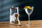 Cocktail in a glass with a lemon twist on a wooden surface, with a dark background.