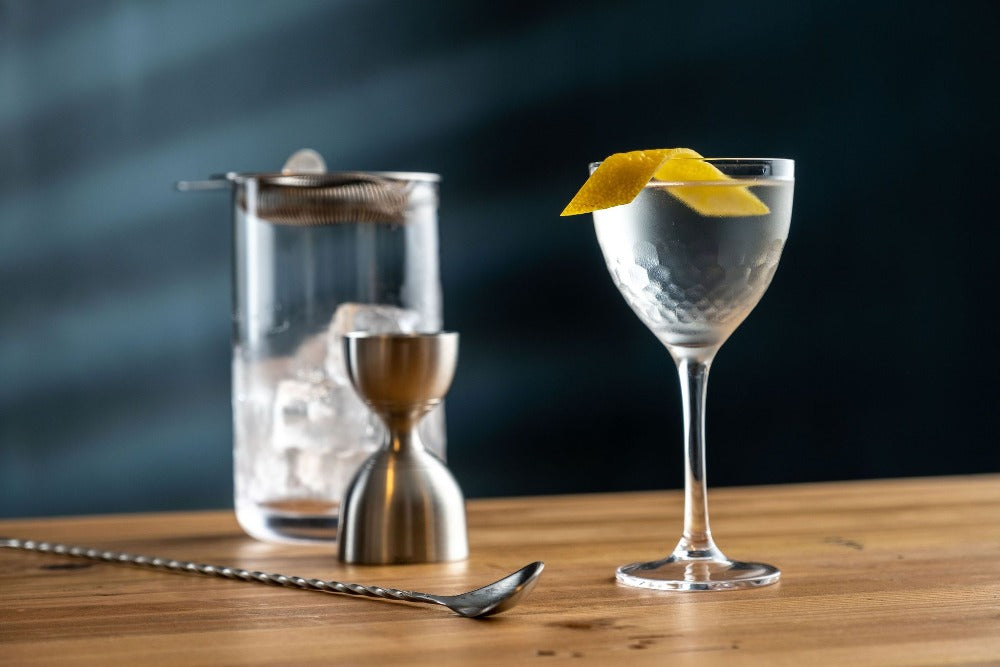 Cocktail in a glass with a lemon twist on a wooden surface, with a dark background.