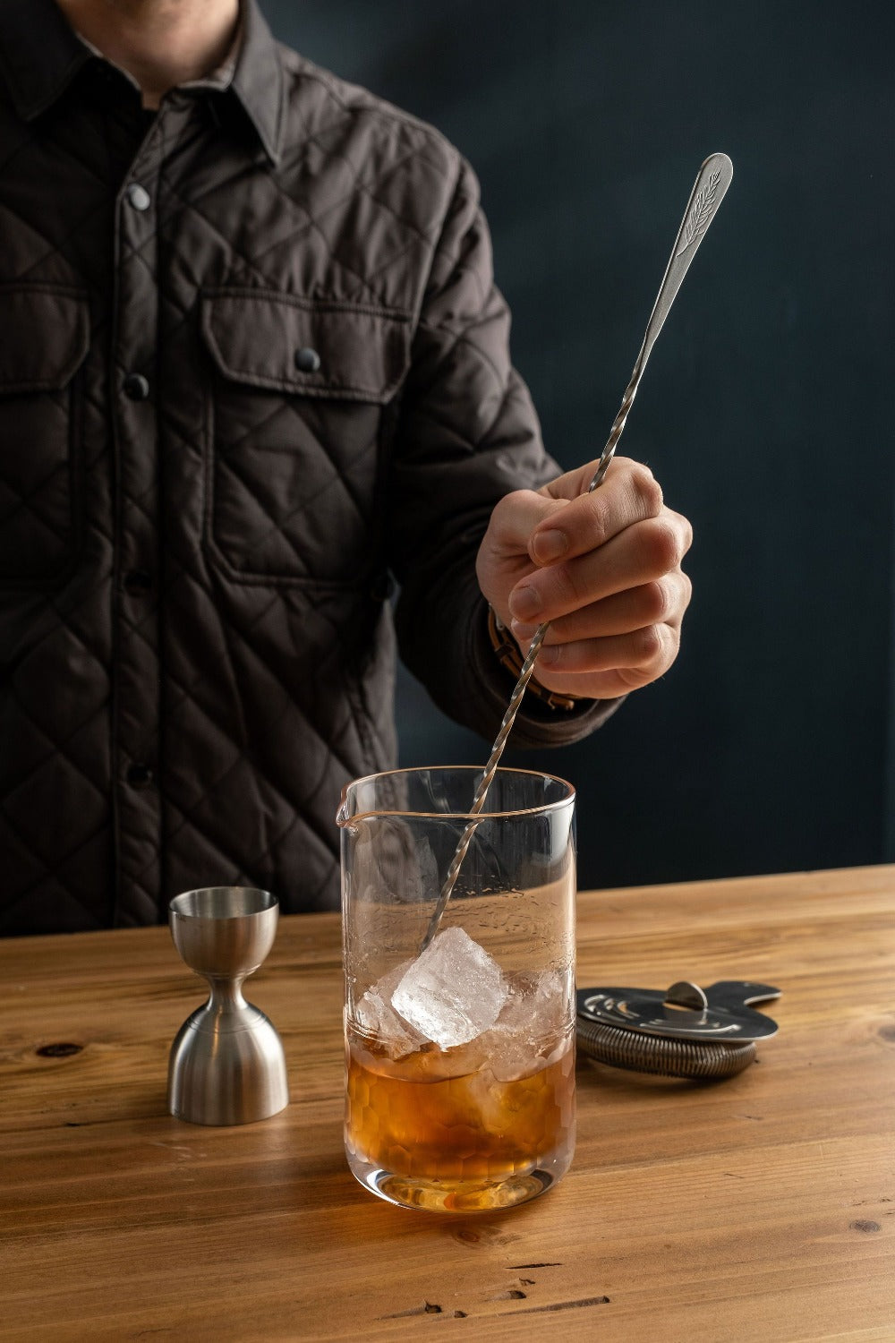 Person stirring a cocktail with a spoon in a glass on a wooden table.
