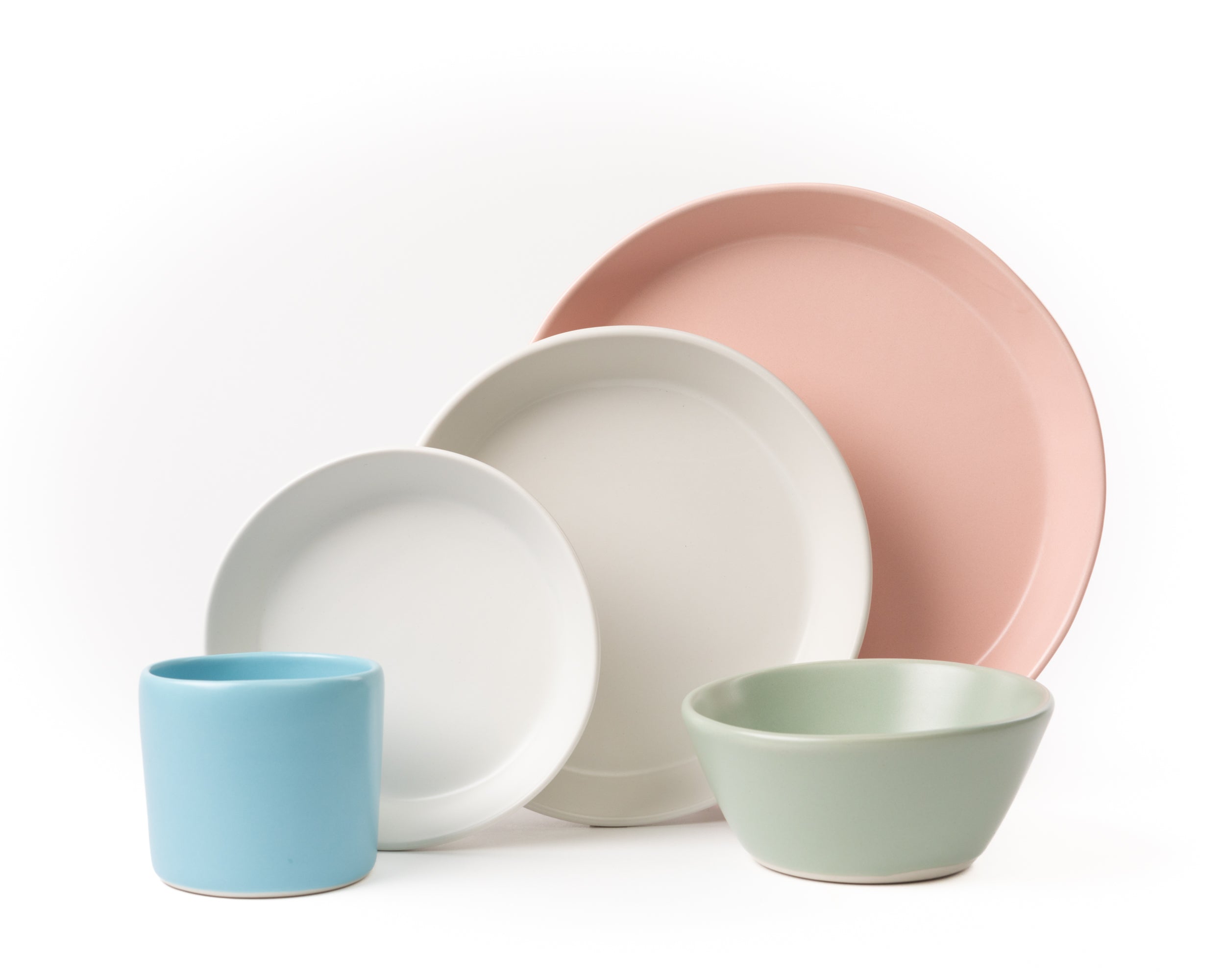 Set of ceramic plates and cups in pastel colors on a white background