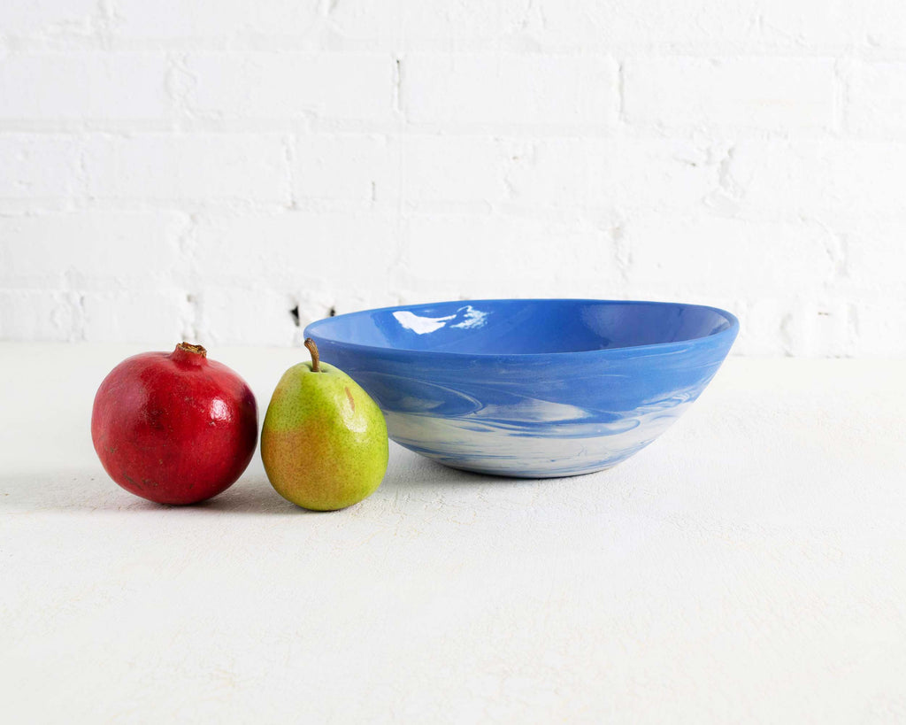 Blue ceramic bowl with a red apple and green pear on a white background