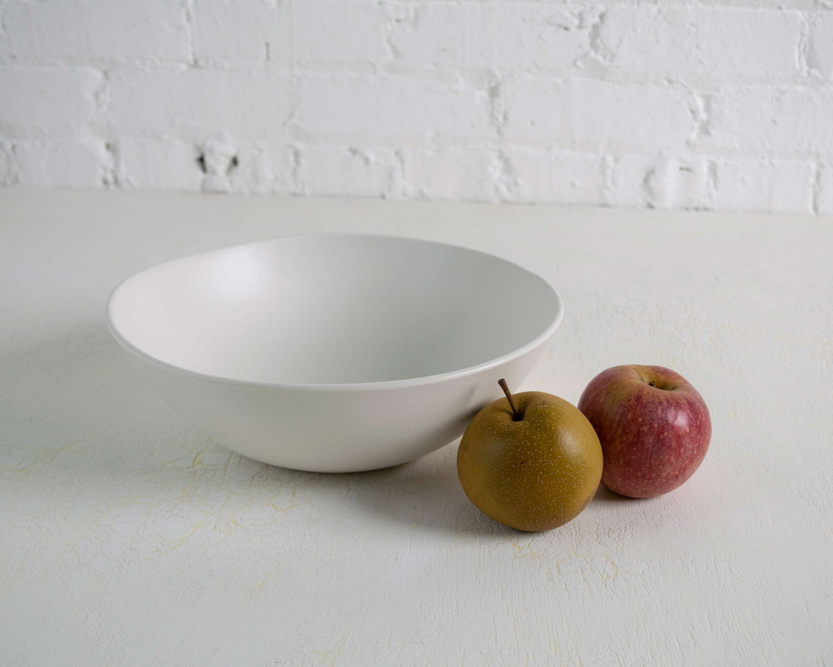 White bowl on a white surface with two apples beside it