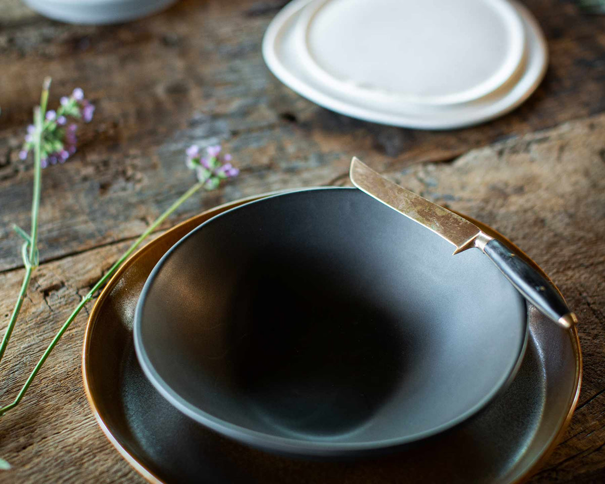 Dark gray bowl on a wooden surface with a small knife and flowers.