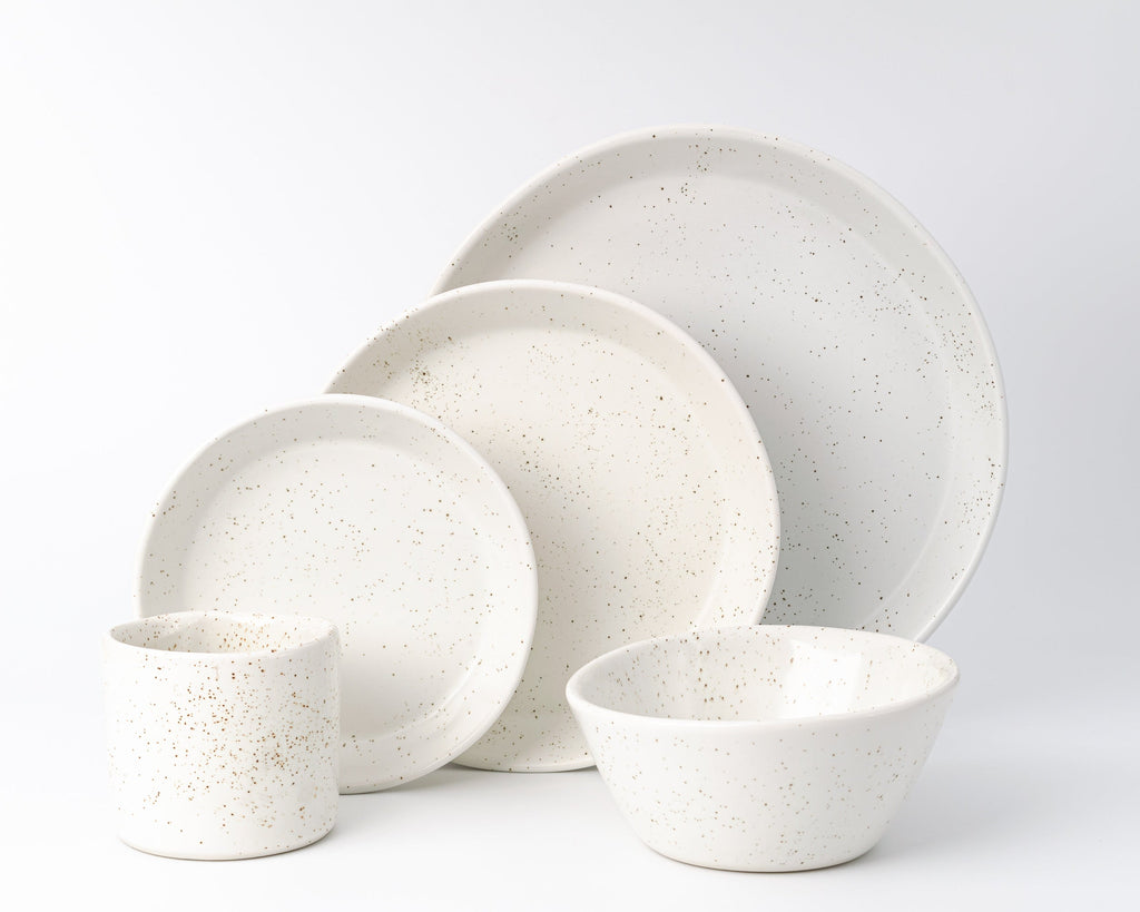 Set of white ceramic dinnerware with speckled texture on a light gray background