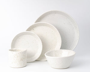 Set of white ceramic dinnerware with speckled texture on a light gray background