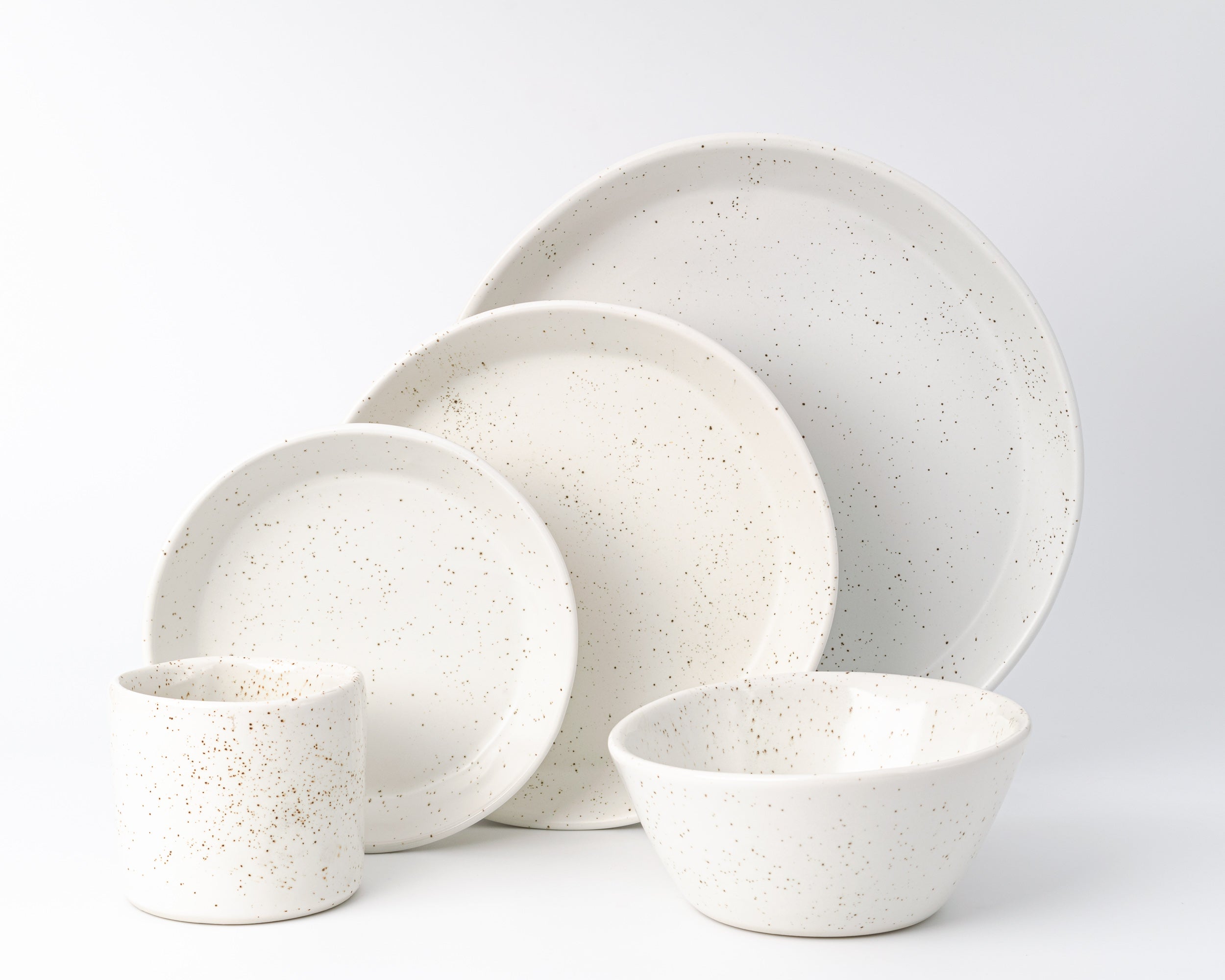 Set of white ceramic dinnerware with speckled texture on a light gray background