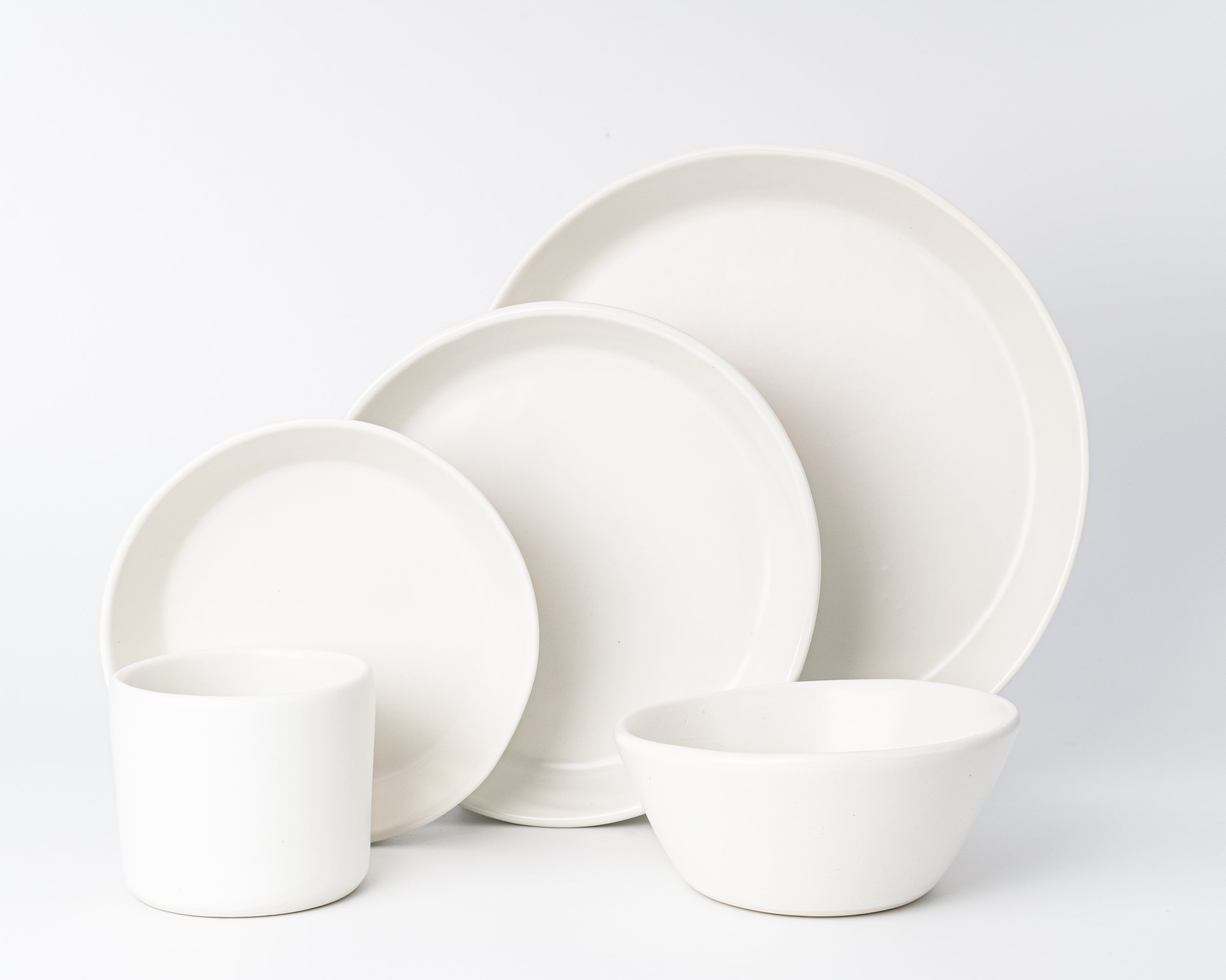 Set of white ceramic dinnerware including plates and bowls on a light gray background