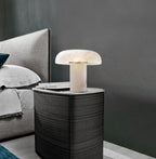 Modern table lamp on a bedside table next to a bed with gray bedding.